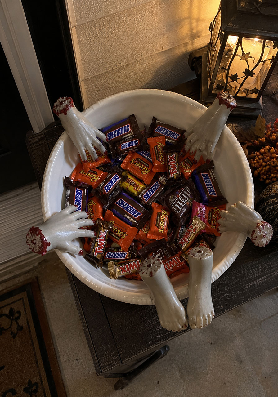 Doll hands and feet arranged around a candy bowl for Halloween trick-or-treat decor