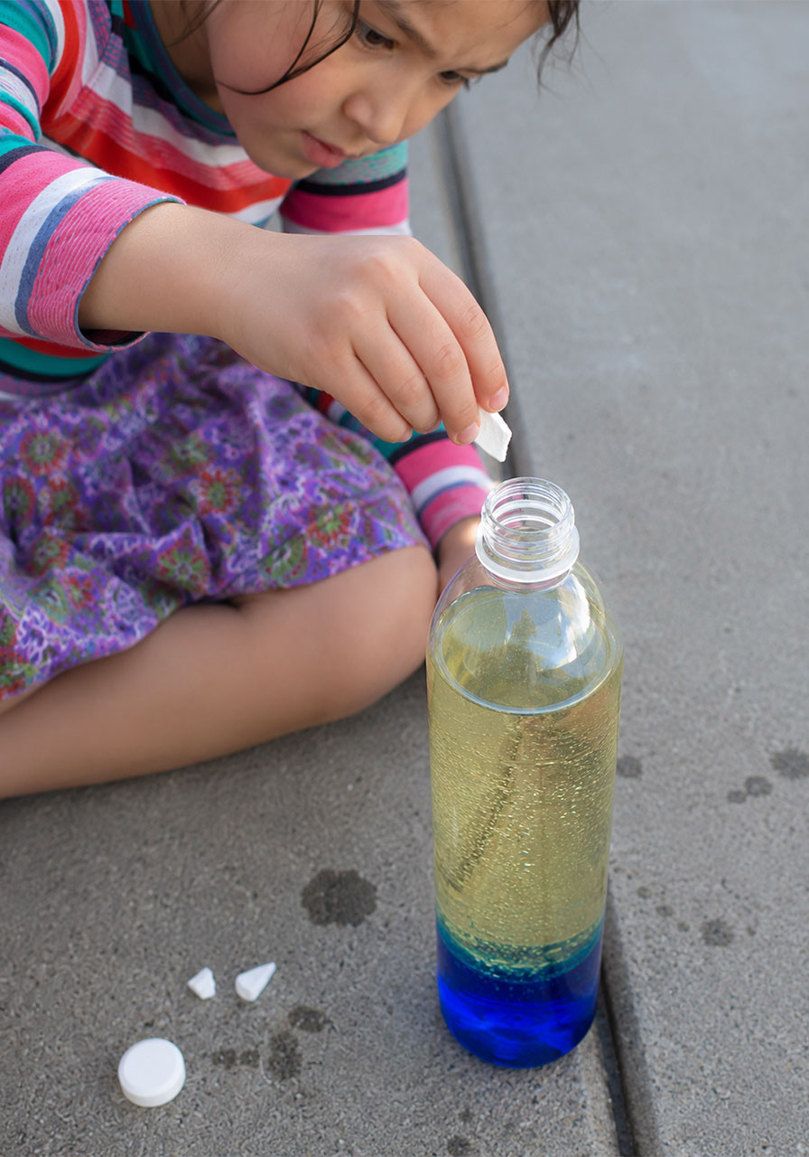 Child dropping Alka-Seltzer tablet piece into DIY lava lamp bottle