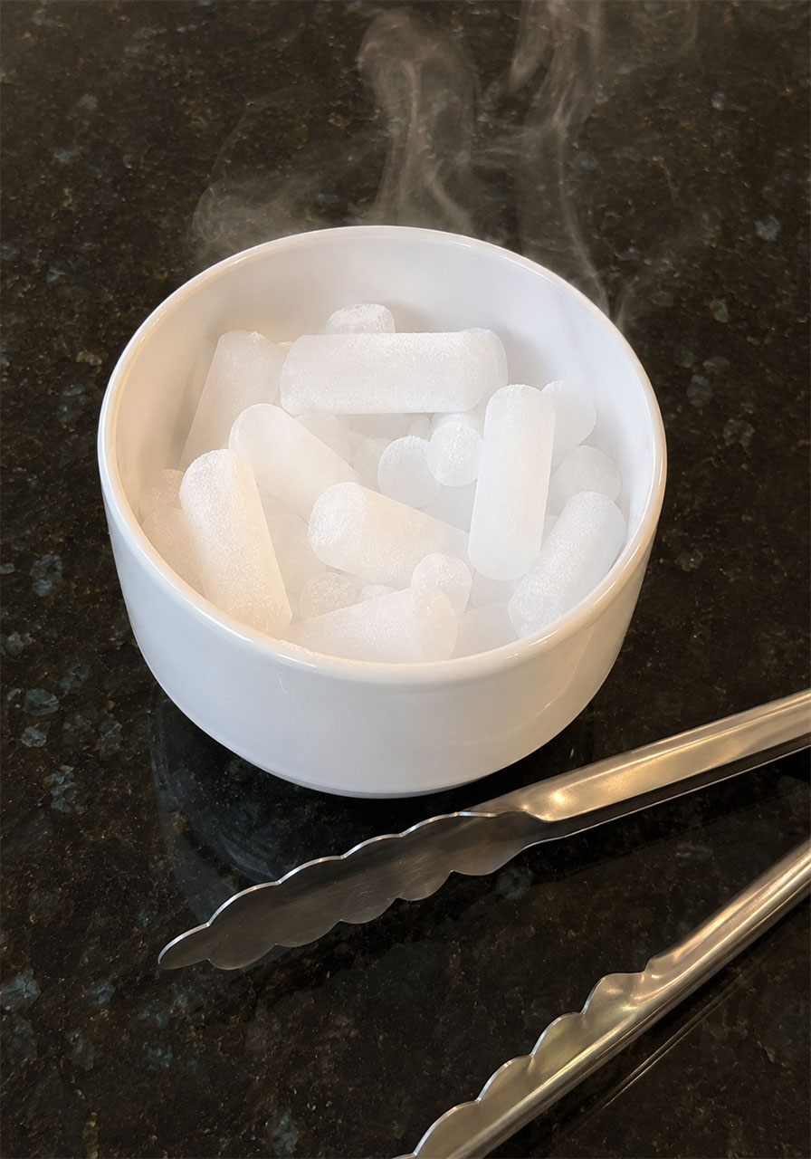 Dry ice pellets in a cup with tongs demonstrating safe handling for Halloween science activity