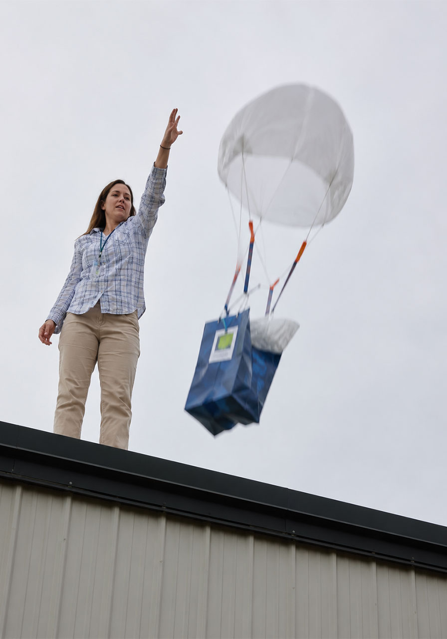 Teacher dropping a parachute egg drop contraption from a school rooftop during testing