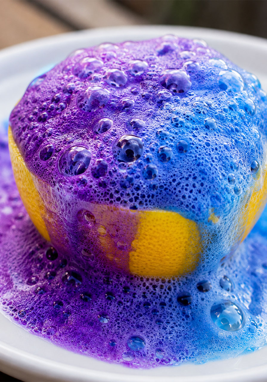 Close-up of foamy chemical reaction bubbling over lemon volcano