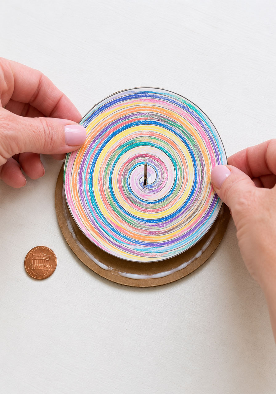 Gluing a colored paper template onto a cardboard circle to make a penny spinner