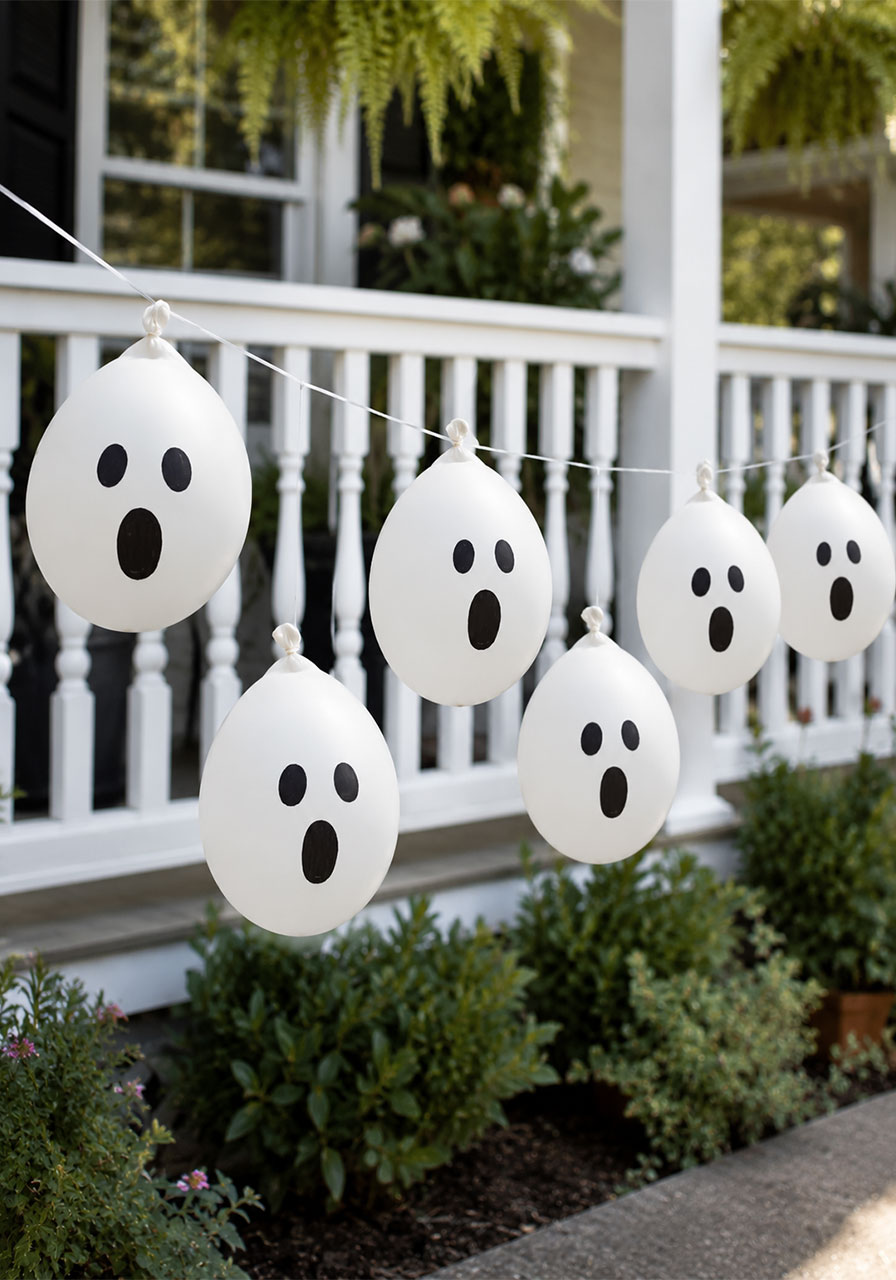White balloon ghost garland with hand-drawn faces decorating a Halloween porch railing