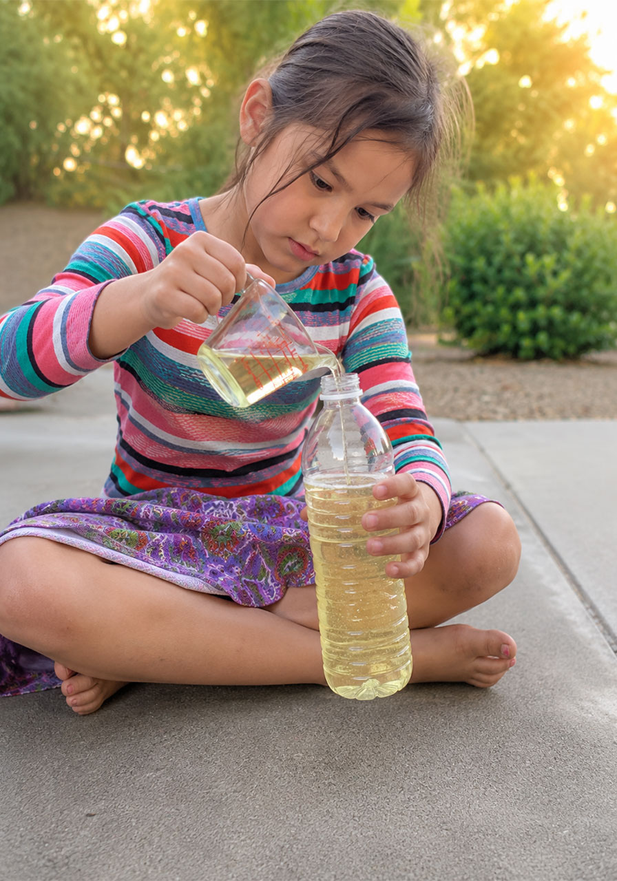 Child pouring vegetable oil into water bottle for homemade lava lamp step one