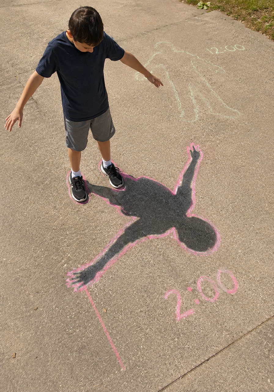 Kids tracing a human sundial shadow with sidewalk chalk as a paper plate sundial variation