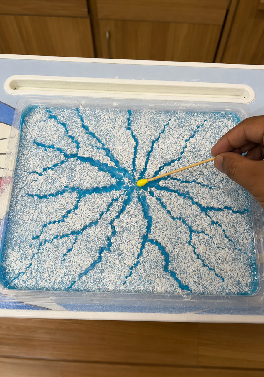 Ice cracking experiment for kids showing blue water surface tension cracks spreading through powder layer