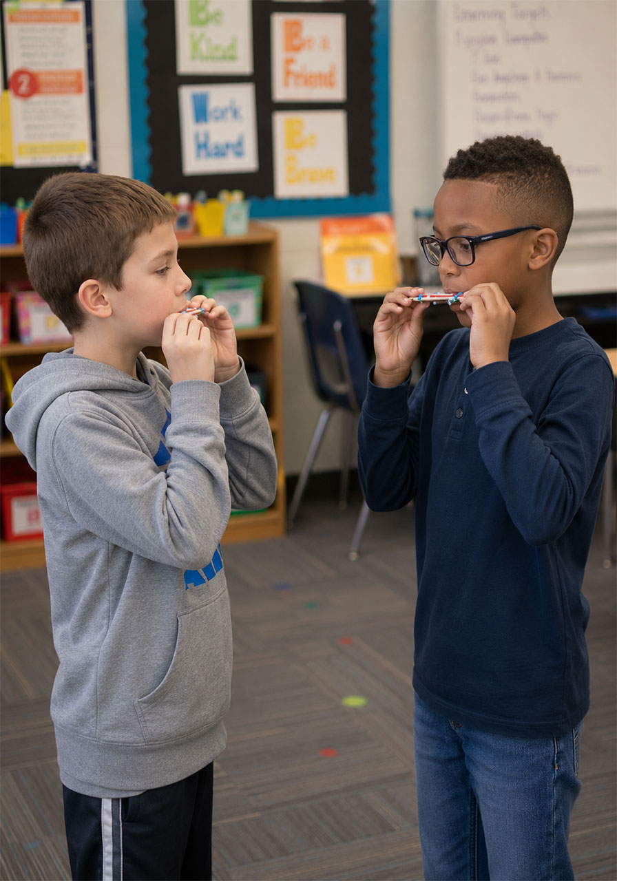 Two kids playing craft stick harmonicas together outdoors