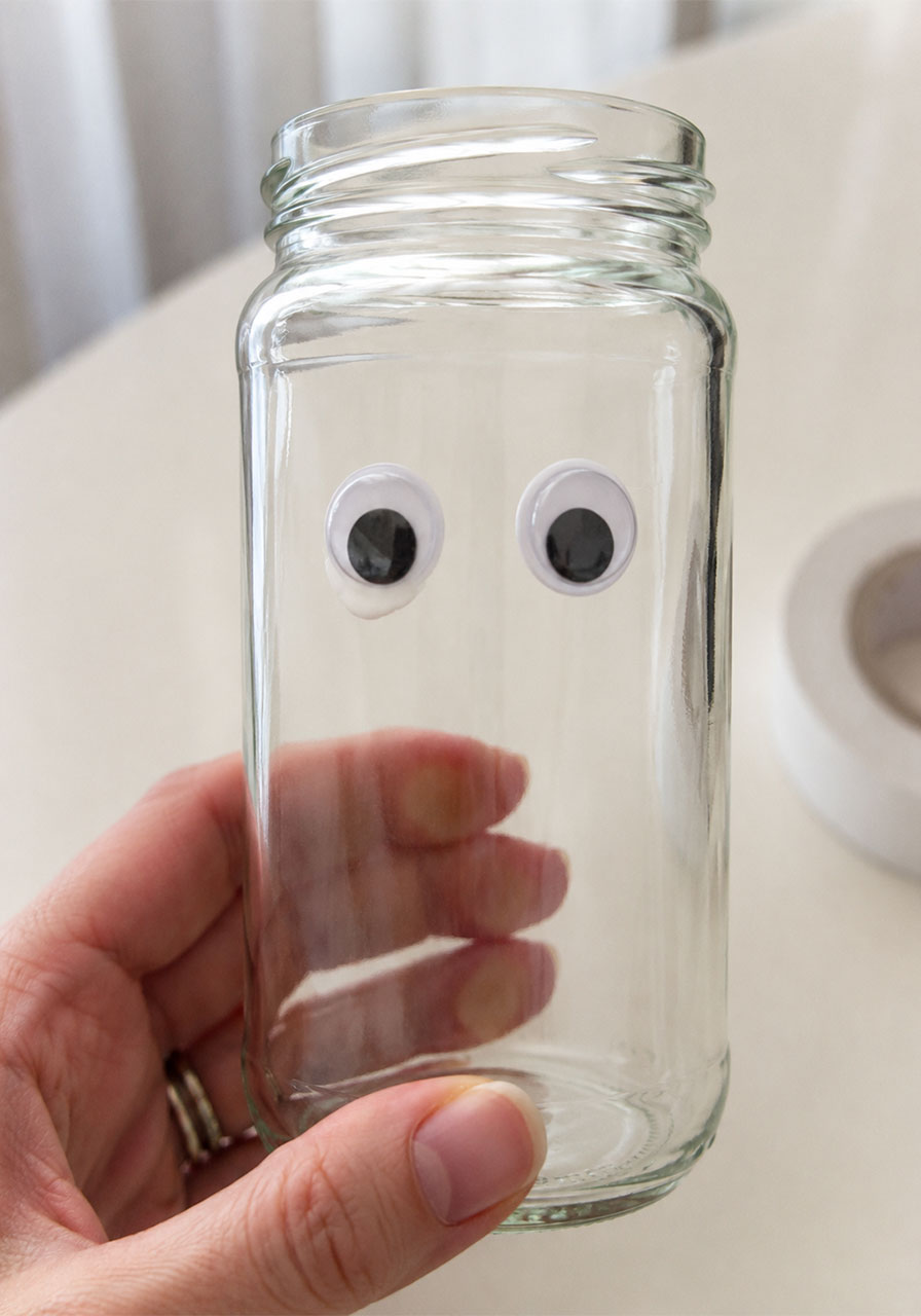 Gluing googly eyes onto glass jar for mummy jar lantern craft step one