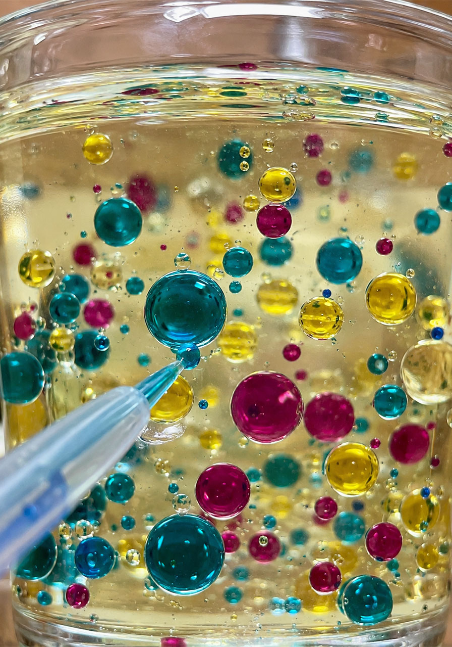 Close-up of colorful water droplets sinking through oil demonstrating density in a science experiment