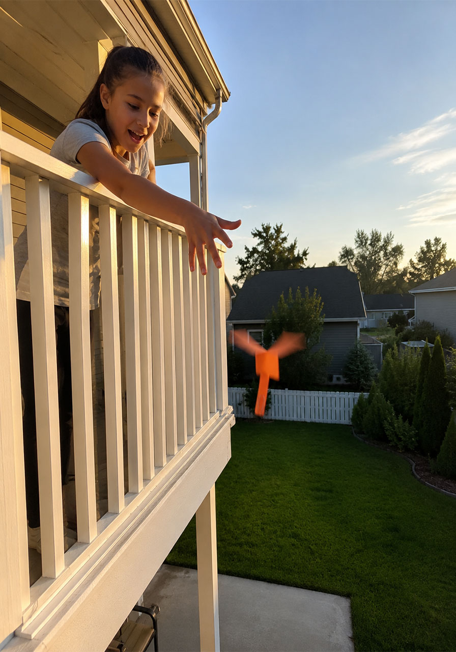 Girl dropping a paper helicopter from a balcony to watch it spin to the ground