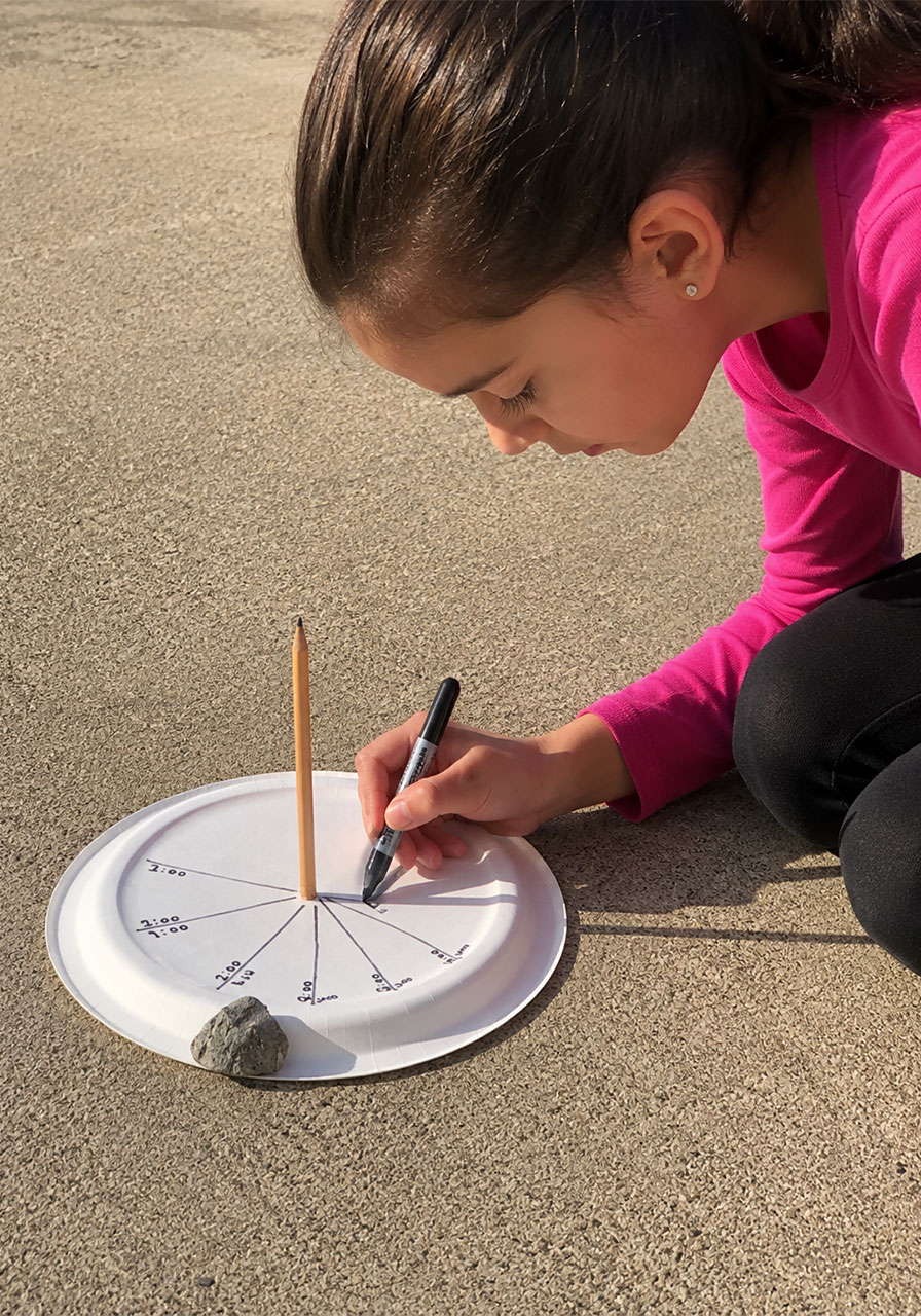 Child marking the hourly shadow line on a paper plate sundial with permanent marker