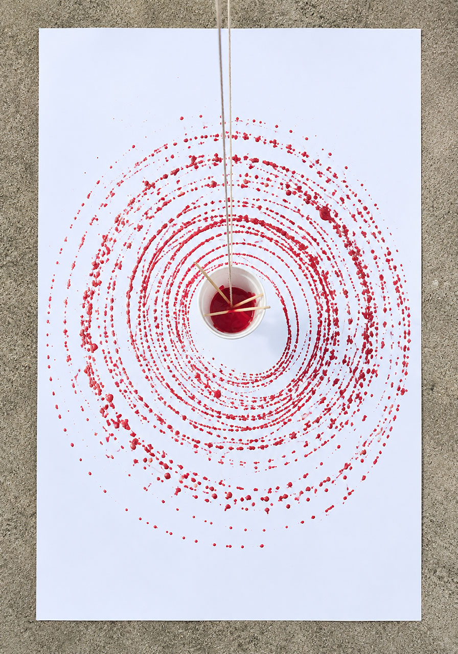 Overhead view of a red paint spiral created by a swinging pendulum