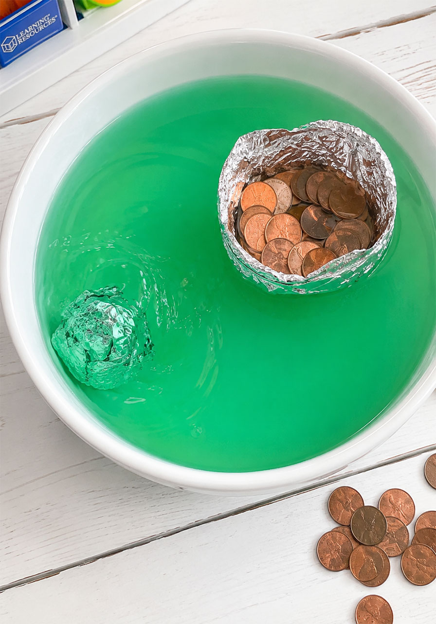 Foil boat filled with pennies floats next to a sinking foil ball in a penny boat challenge STEM experiment