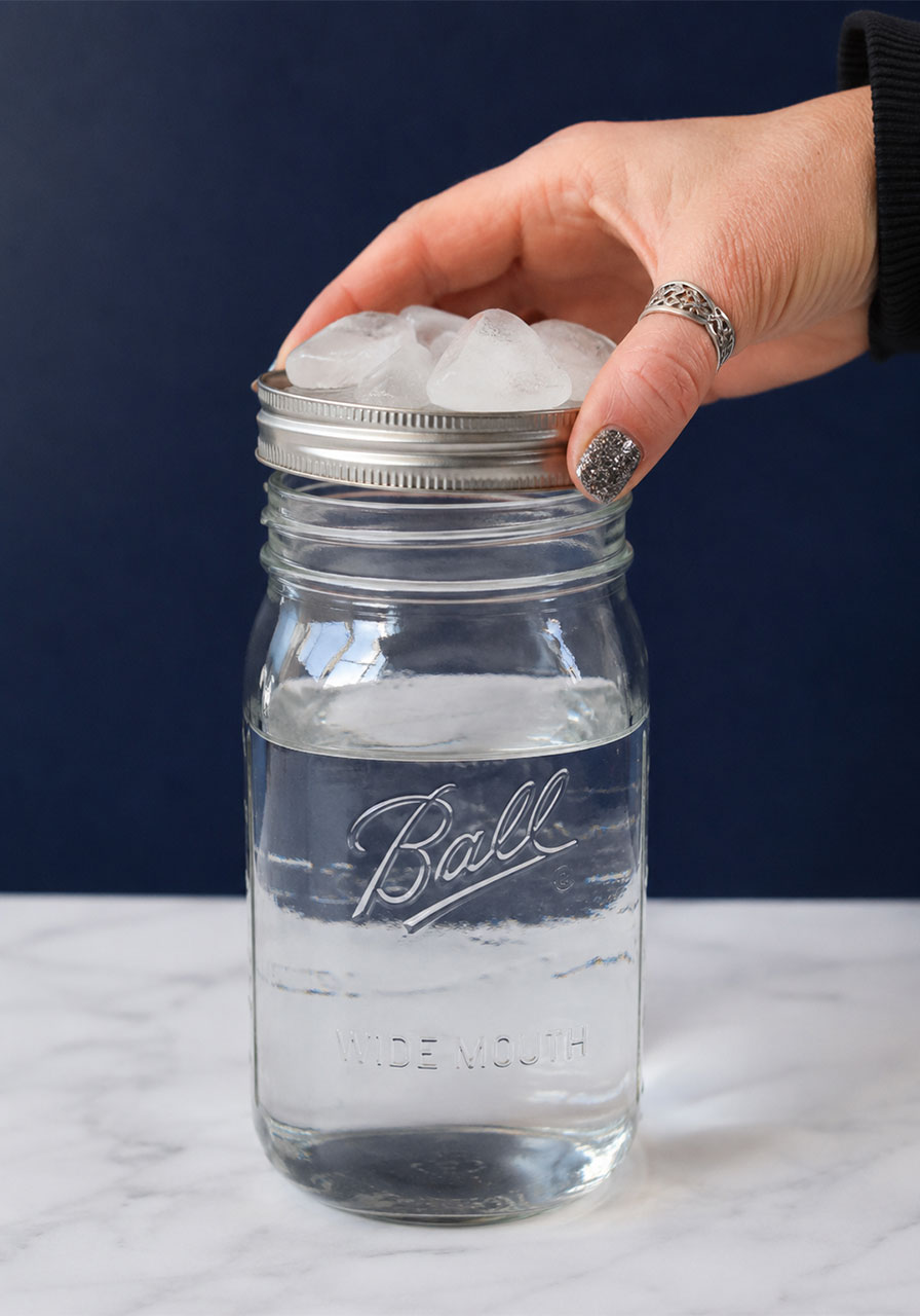 Placing ice-filled lid onto mason jar during cloud experiment for kids