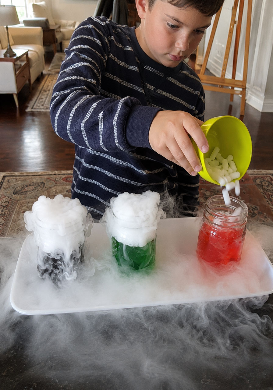 Child pouring dry ice into a jar of red colored water creating a bubbling Halloween potion
