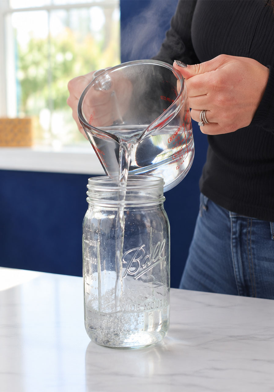 Adult pouring warm water into mason jar for cloud in a jar experiment