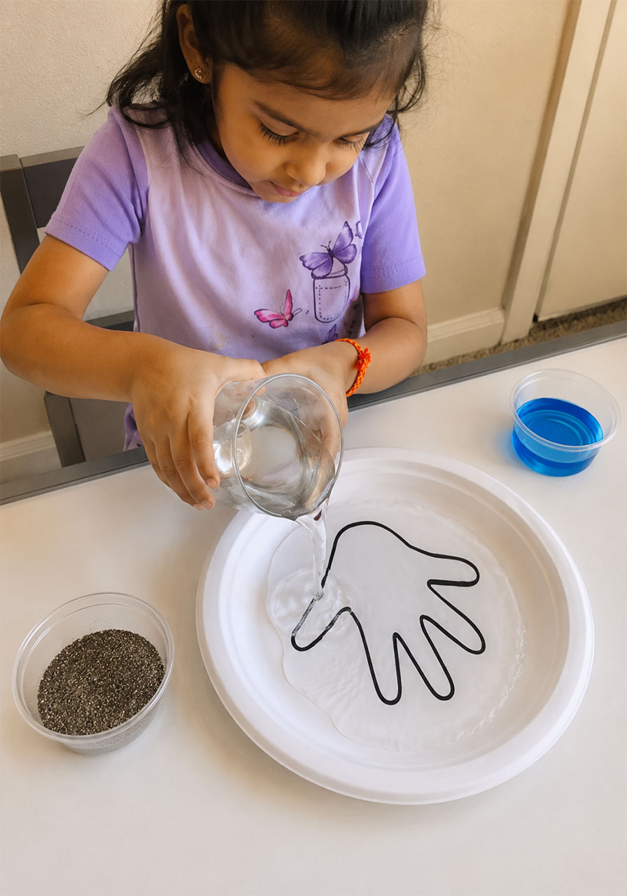 Toddler pouring water onto a traced hand outline for the soap and pepper science experiment