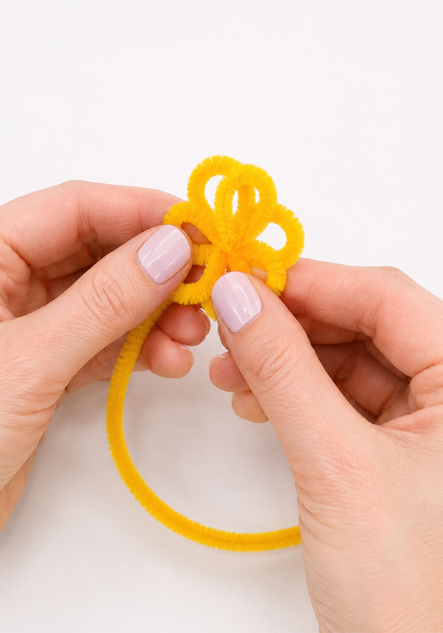 Hands shaping a yellow pipe cleaner into a flower shape before making borax crystals