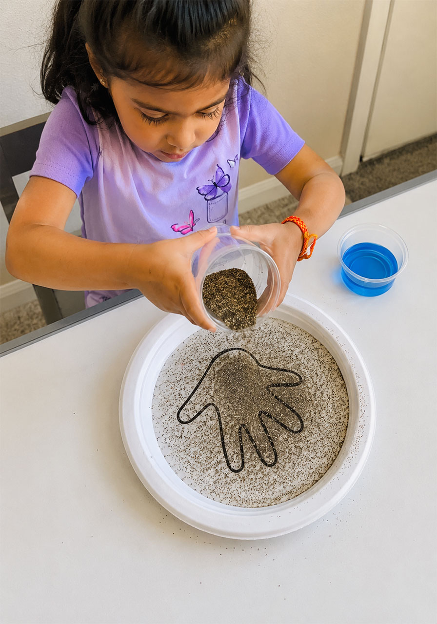 Toddler sprinkling pepper into water to represent germs before the soap experiment