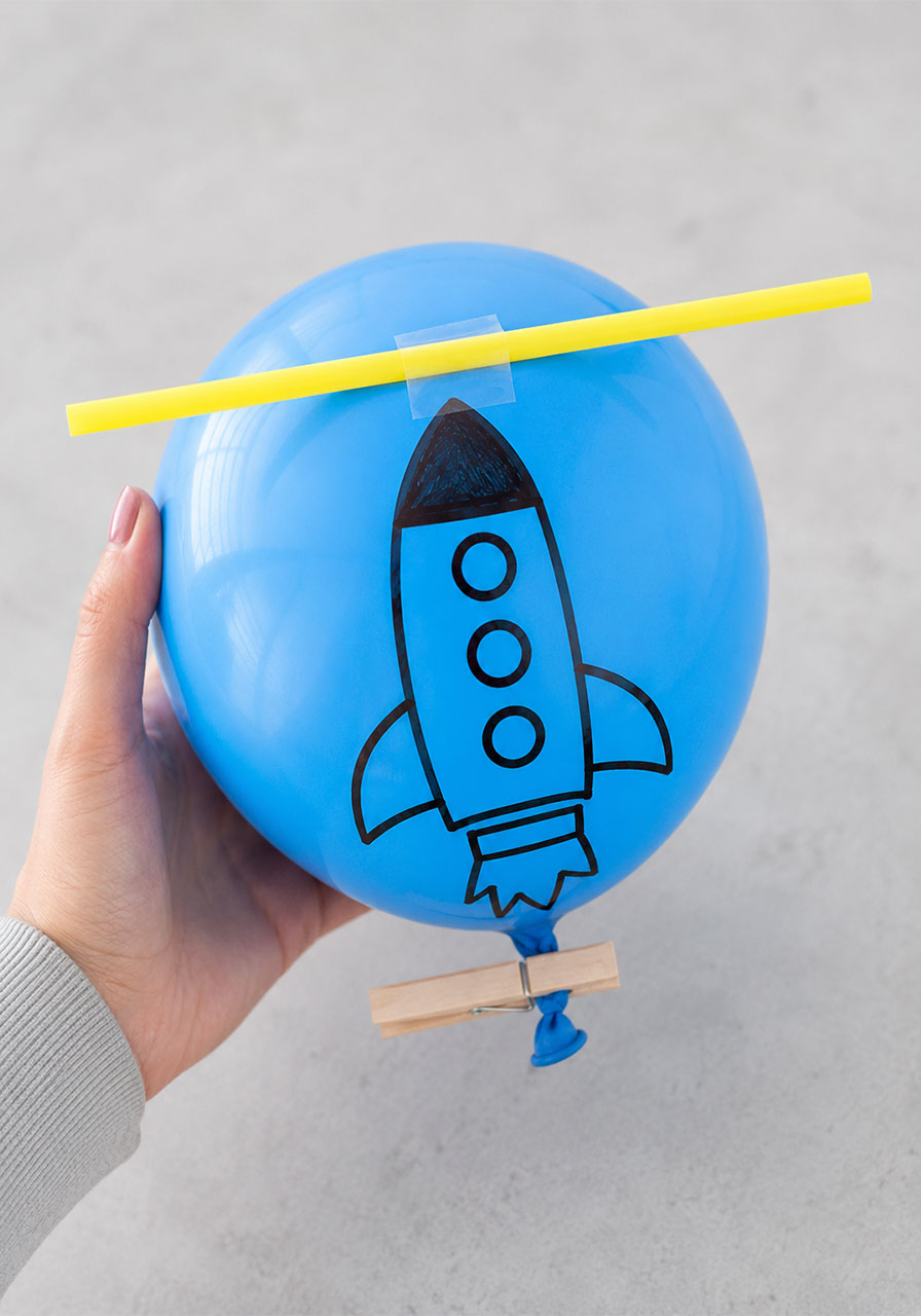 Taping a plastic straw to a decorated balloon to build a simple balloon rocket
