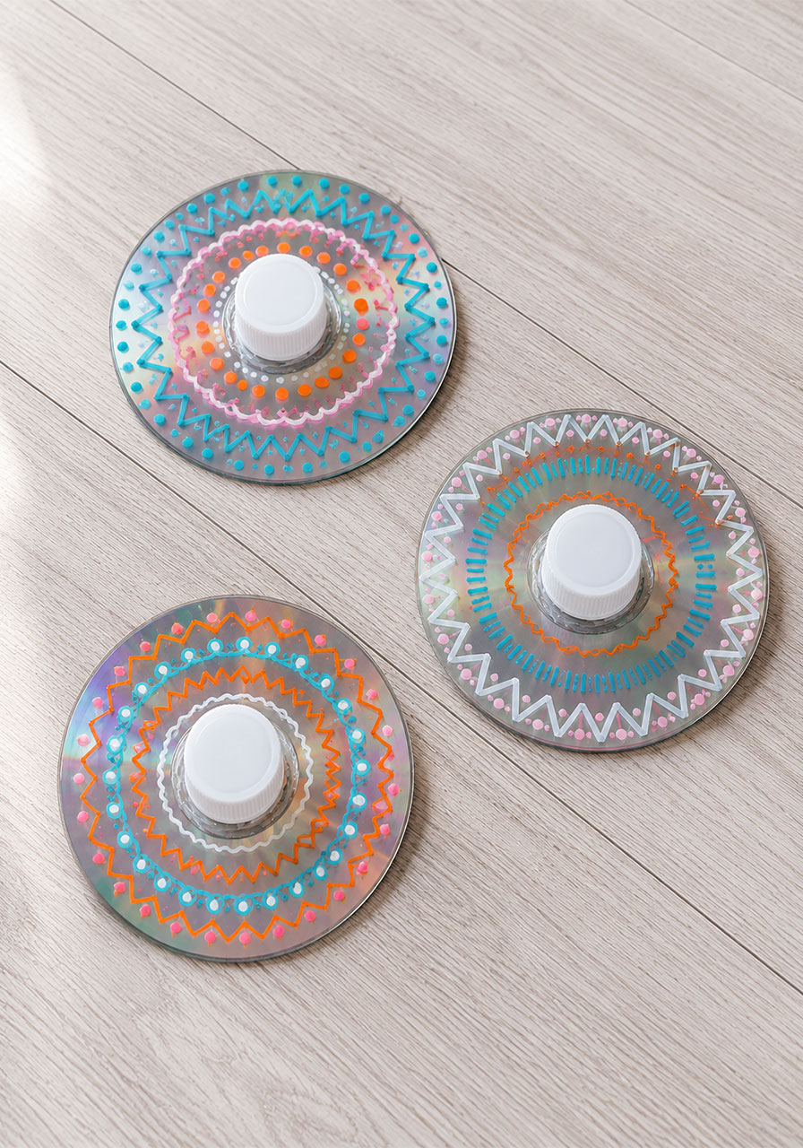 Three finished homemade CD spinning tops decorated with colorful chalk marker designs