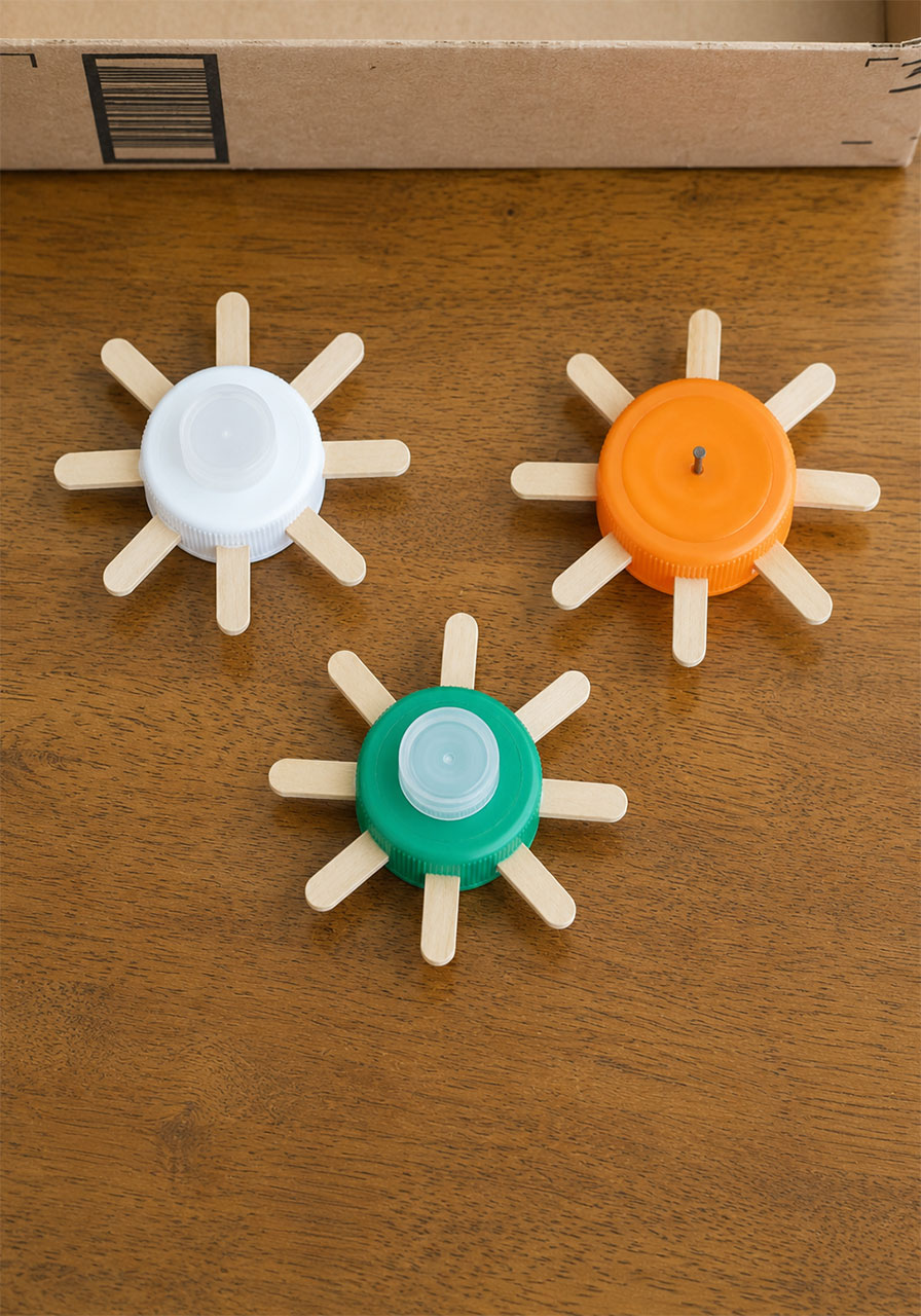 Three finished DIY gears made from popsicle sticks and bottle caps ready to be mounted in a STEM activity box