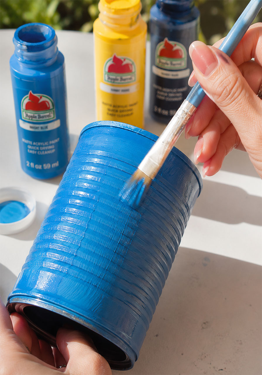 Painting a bright blue acrylic base coat onto a tin can for a wind chime STEM craft