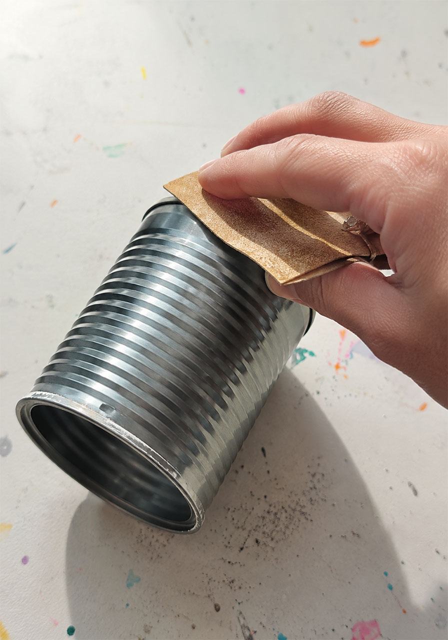 Sanding the sharp edge of a metal can to prepare it safely for a wind chime STEM project