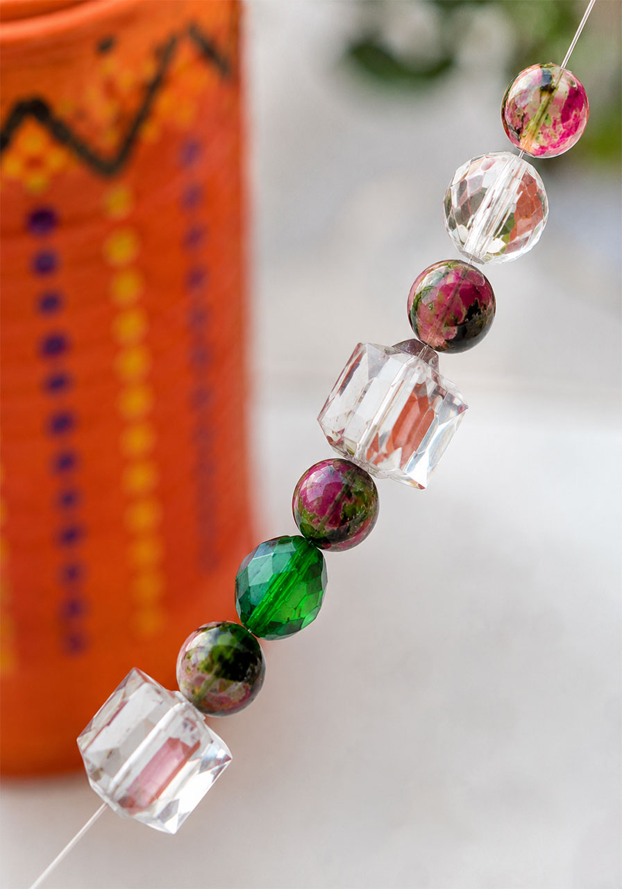 Threading colorful glass beads onto string for a tin can wind chime craft