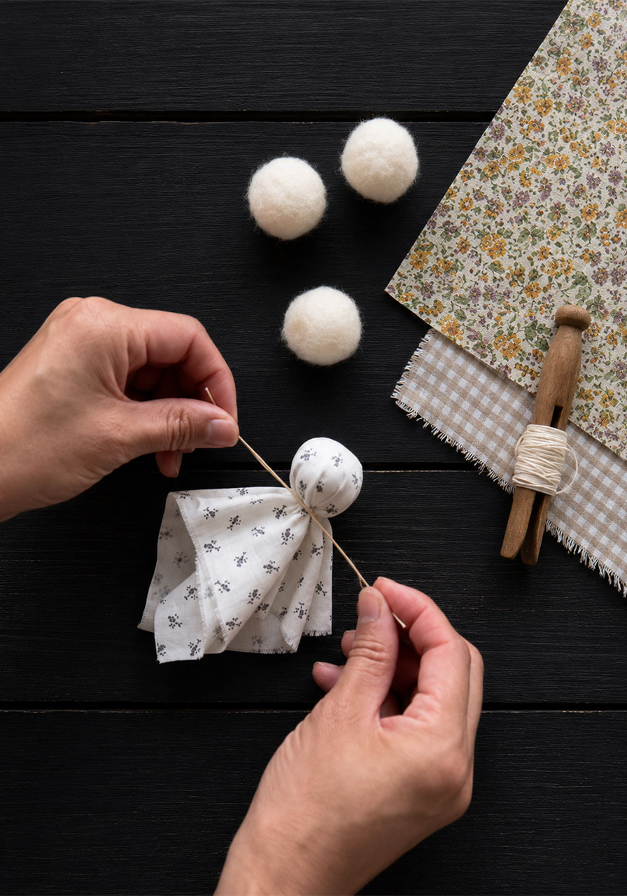 Tying twine around a fabric ghost's neck during assembly