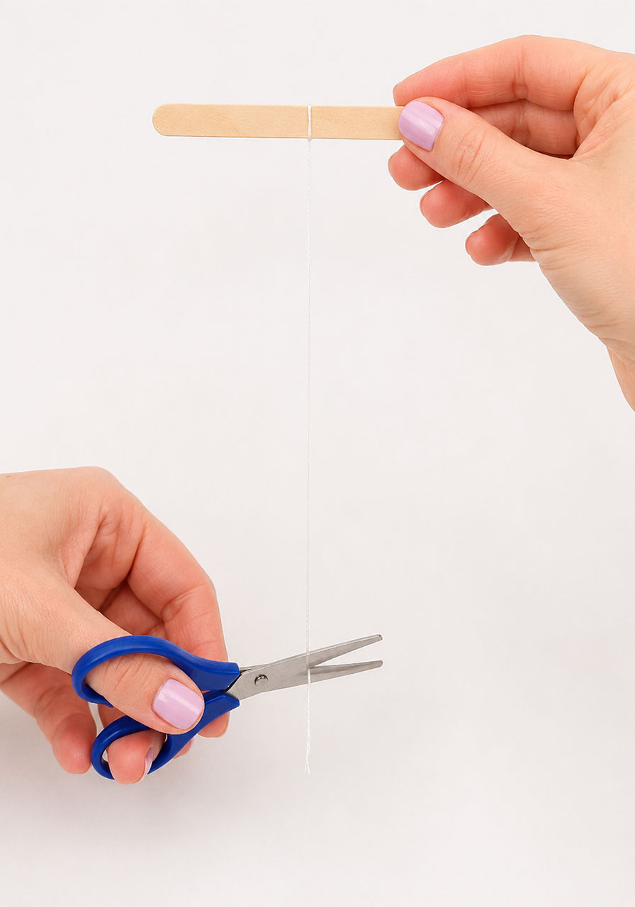 Tying thread to a popsicle stick to suspend the pipe cleaner shape in the jar
