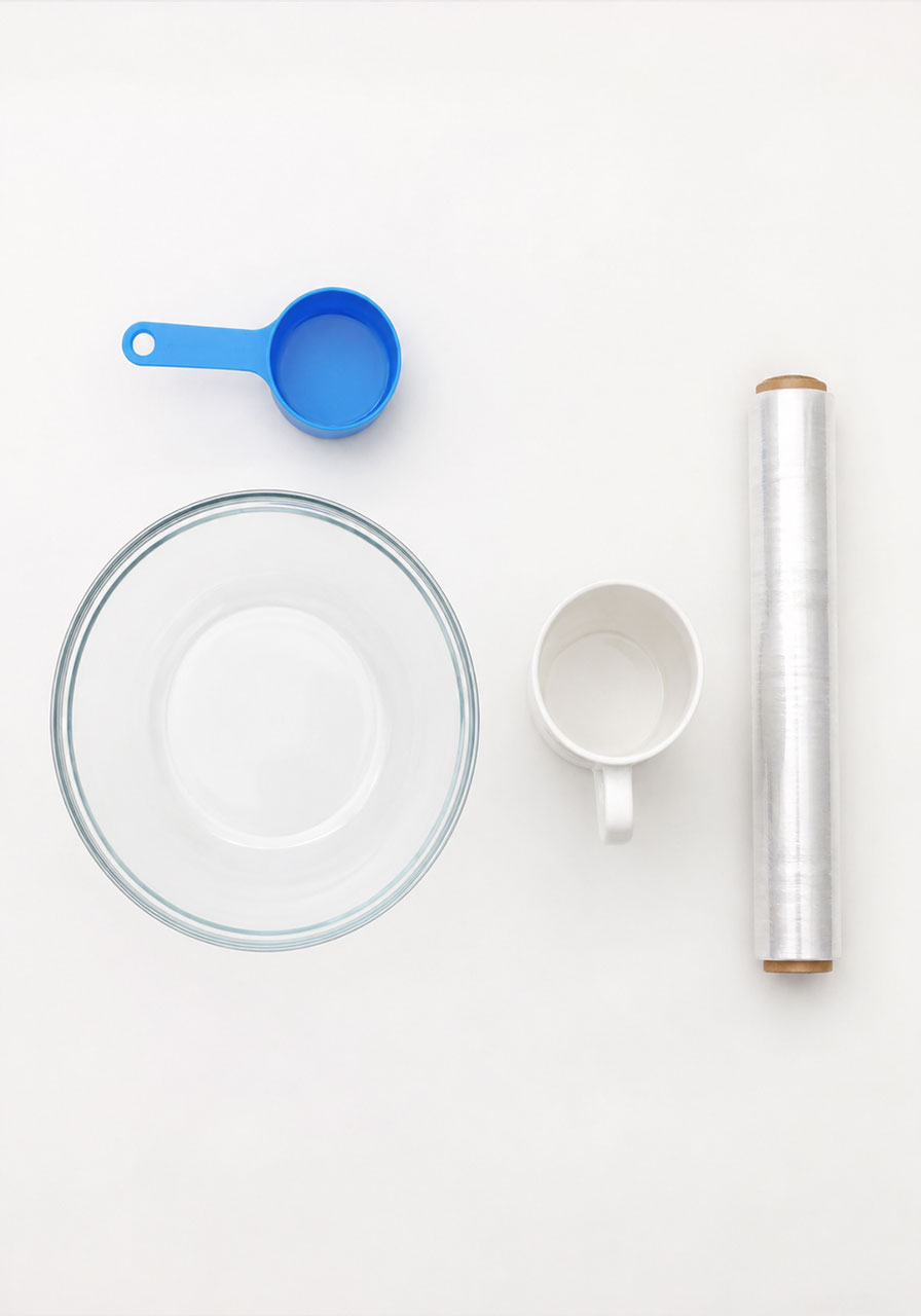 Supplies needed for the water cycle bowl experiment including a bowl, mug, plastic wrap, and water