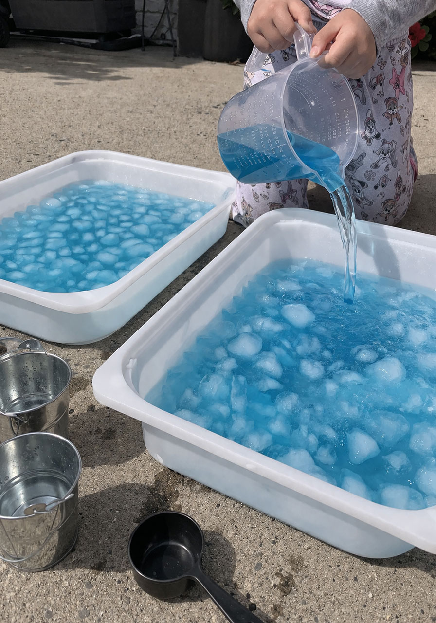 Child pouring colored water into ice bin for fine motor scooping and pouring sensory play